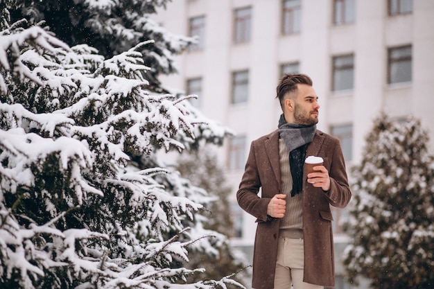 Bezpłatne zdjęcie młody przystojny mężczyzna pije gorącą kawę outside na zima dniu