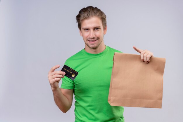 Młody przystojny mężczyzna ubrany w zielony t-shirt, trzymając pakiet papieru i kartę kredytową