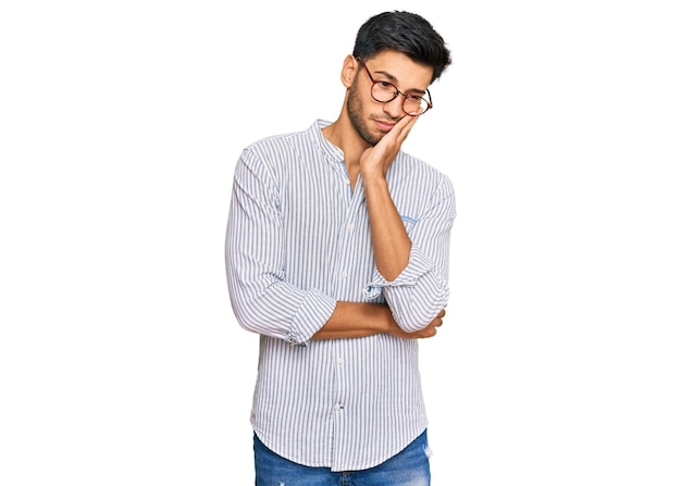 Bezpłatne zdjęcie młody przystojny mężczyzna ubrany w zwykłe ubrania i okulary, myślący, wyglądający na zmęczonego i znudzonego problemami z depresją ze skrzyżowanymi ramionami