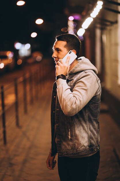 Młody przystojny mężczyzna używa telefon przy nocą w ulicie