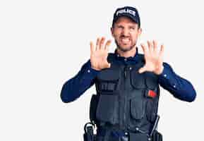 Bezpłatne zdjęcie młody przystojny mężczyzna w mundurze policyjnym uśmiechający się zabawnie wykonujący gest pazurów jako kot, agresywny i seksowny wyraz twarzy