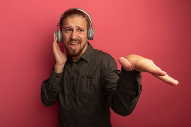 Młody przystojny mężczyzna w szarej koszuli ze słuchawkami na głowie, niezadowolony z wyciągniętym ramieniem