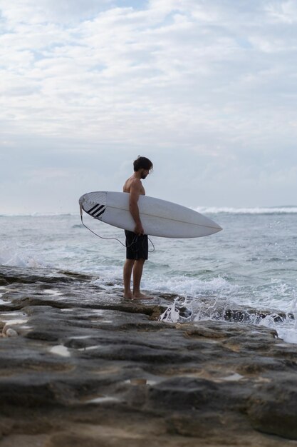 Młody przystojny mężczyzna z deską surfingową na oceanie.
