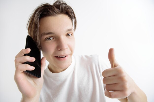 Młody przystojny nastolatek pokazuje ekran smartfona i podpisuje znak OK na białym tle na szarym tle. Ludzkie emocje, wyraz twarzy, koncepcja reklamy.