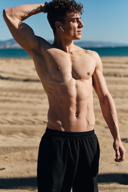 Młody przystojny sportowy mężczyzna z nagim torsem odpoczywa po treningu na świeżym powietrzu. Atrakcyjny męski model fitness pozuje na plaży