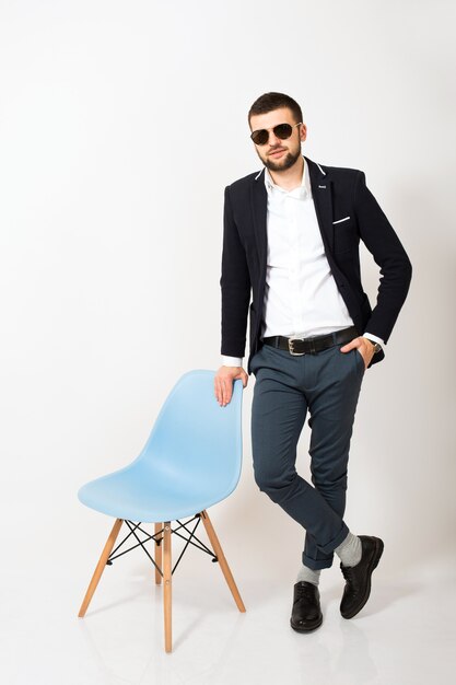 Młody przystojny stylowy hipster mężczyzna w czarnej kurtce, styl biznesowy, biała koszula, na białym tle, białe tło, uśmiechnięty, atrakcyjny, pełnej wysokości, wyglądający pewnie i fajnie, pozuje z krzesłem biurowym