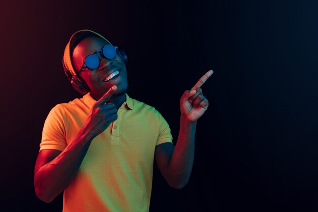 Młody przystojny szczęśliwy hipster mężczyzna słuchanie muzyki w słuchawkach na czarno z neonów