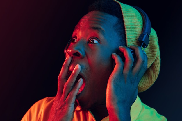 Młody przystojny szczęśliwy hipster zaskoczony mężczyzna słuchanie muzyki w słuchawkach w czarnym studio