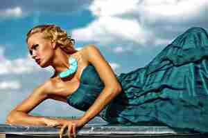 Bezpłatne zdjęcie młody seksowny blond kobieta model w wieczór sukni pozuje na niebieskiego nieba tle
