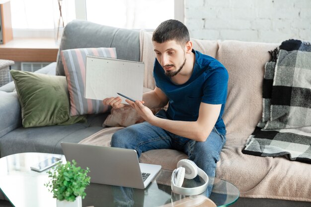 Młody skupiony mężczyzna uczący się w domu podczas kursów online lub samodzielnych bezpłatnych informacji