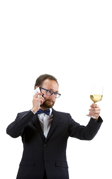 Młody sommelier polerujący kieliszek do wina, rozmawiając telefon na białym tle.