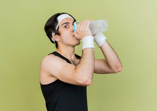 Młody sportowy człowiek ubrany w sportową wodę pitną i pałąk po treningu