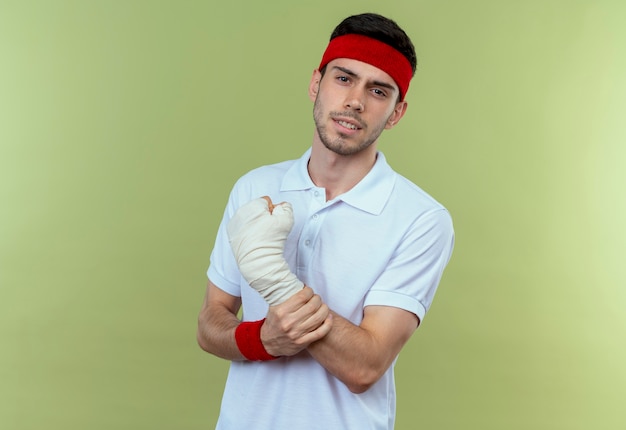 Młody sportowy mężczyzna w opasce dotykając zabandażowanego nadgarstka czuje ból na zielono