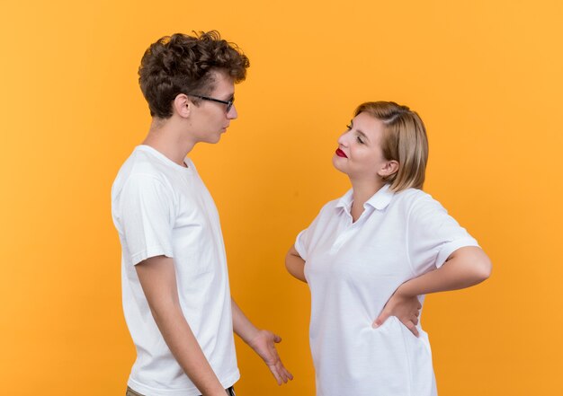 Młody sportowy para mężczyzna i kobieta patrząc na siebie, argumentując, stojąc nad pomarańczową ścianą