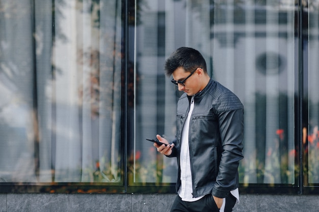 Młody stylowy facet w okularach w czarnej skórzanej kurtce z telefonem na powierzchni szkła