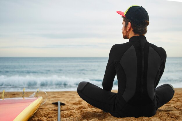 Młody surfer mężczyzna na plaży w czapce