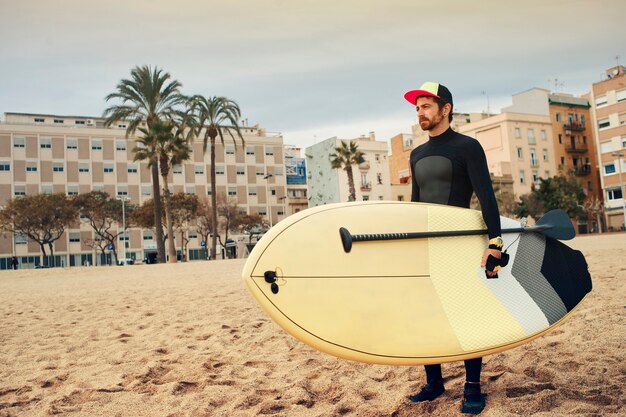 Młody surfer mężczyzna na plaży z deską surfingową