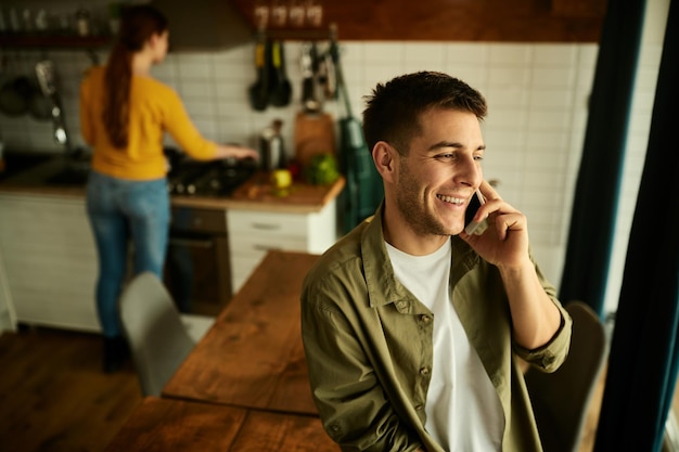 Młody szczęśliwy człowiek rozmawia przez telefon komórkowy w domu