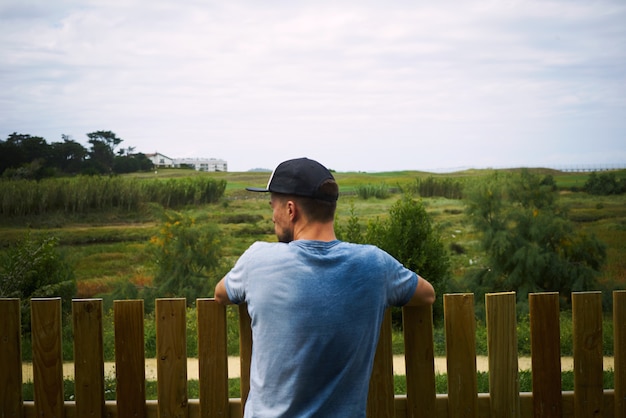 Młody turysta patrząc na zielony krajobraz stojący ogrodzeniem