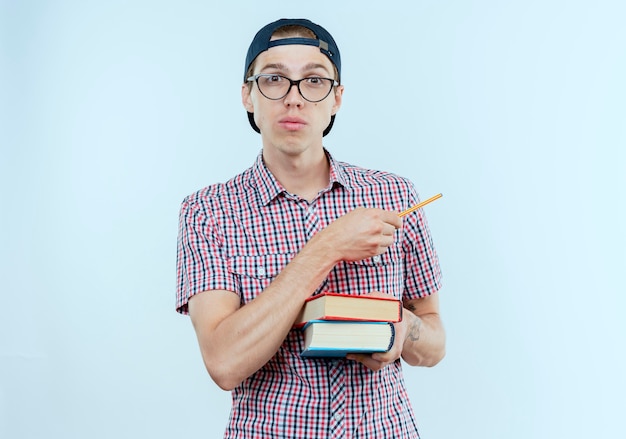 młody uczeń chłopiec w okularach i czapce, trzymając książki i wskazuje na bok piórem