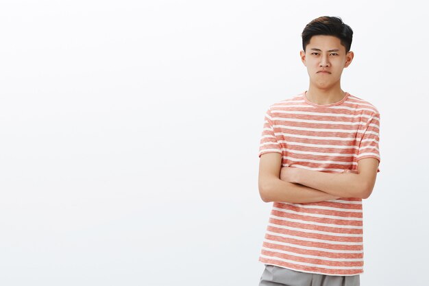 Młody uroczy Chińczyk w pasiastej koszulce wygląda na obrażonego i wściekłego, trzymając w środku zniewagę