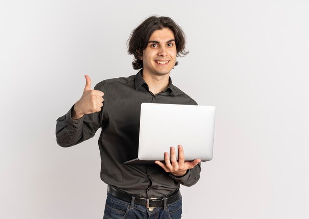 Młody uśmiechnięty przystojny kaukaski mężczyzna trzyma laptopa i kciuki do góry na białym tle na białym tle z miejsca na kopię