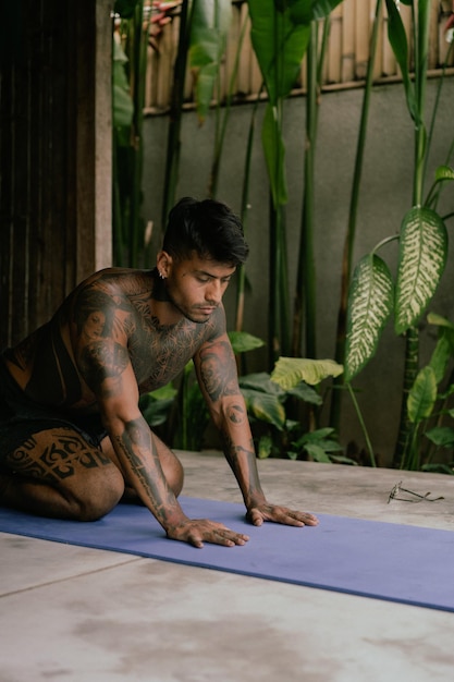 Młody wytatuowany mężczyzna z Ameryki Łacińskiej ćwiczy jogę na świeżym powietrzu podczas wakacji rekolekcyjnych na Bali, rozciąganie, medytacja, wellness