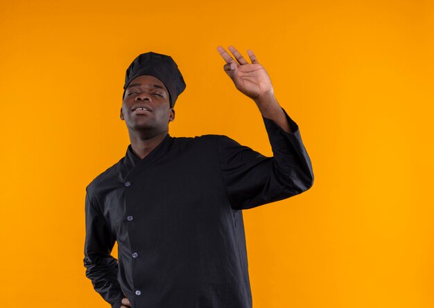 Młody zadowolony afro-amerykański kucharz w mundurze szefa kuchni gestów ok ręka znak na białym tle na pomarańczowym tle z miejsca na kopię