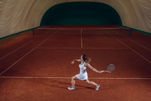 Młody zawodowy sportsmenka, grając w tenisa na ścianie boisko sportowe