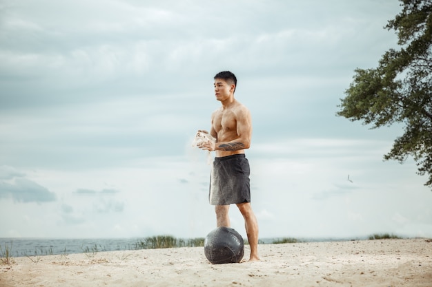 Młody zdrowy mężczyzna sportowiec robi ćwiczenia z piłką na plaży