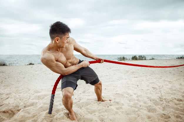 Młody zdrowy mężczyzna sportowiec robi przysiady na plaży