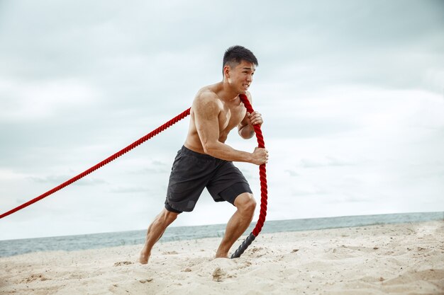 Młody zdrowy mężczyzna sportowiec robi przysiady na plaży