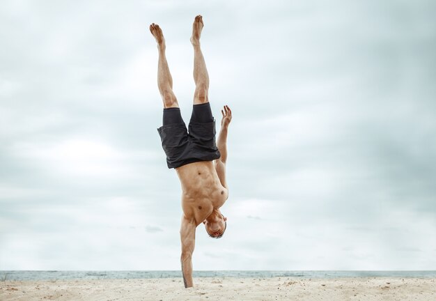 Młody zdrowy mężczyzna sportowiec robi przysiady na plaży