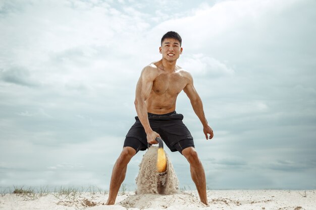 Młody zdrowy mężczyzna sportowiec robi przysiady na plaży