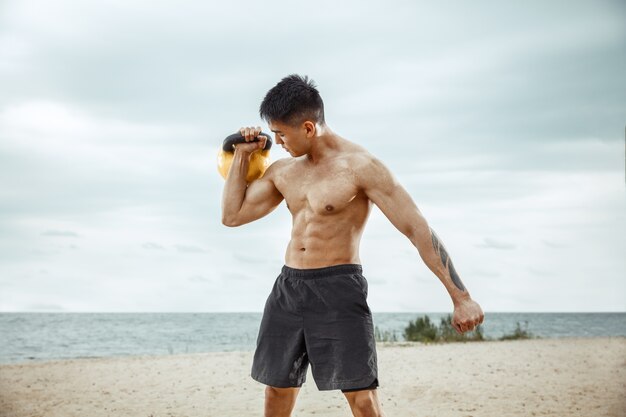 Młody zdrowy mężczyzna sportowiec robi przysiady na plaży