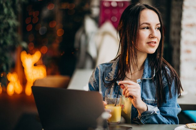 Młody żeński uczeń pracuje na laptopie w barze i je pizzę