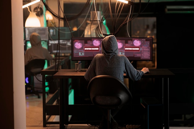 Bezpłatne zdjęcie młody złodziej próbujący włamać się do systemu komputerowego na wielu monitorach, używając złośliwego oprogramowania serwerowego do rozmieszczenia wirusów. niebezpieczny haker wyłudzający informacje i popełniający cyberterroryzm, kradnący hasła.