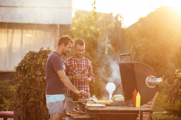 Bezpłatne zdjęcie młodzi człowiecy piec grilla na grillu w wiejskiej chałupy.