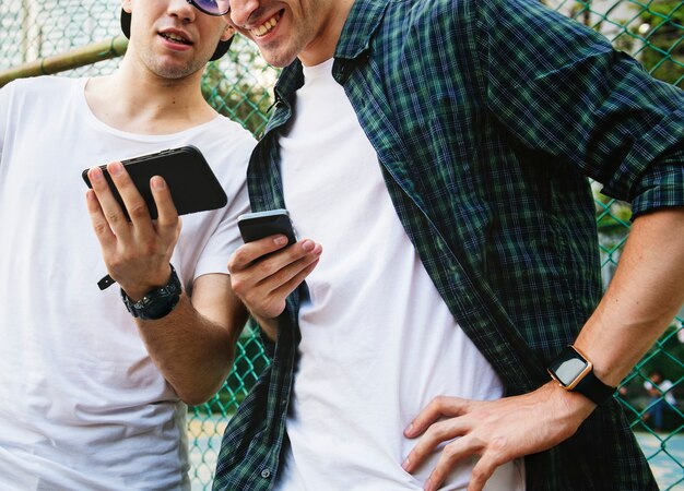 Młodzi dorosli męscy przyjaciele na boisko do koszykówki używać smartphones millennials pojęcie
