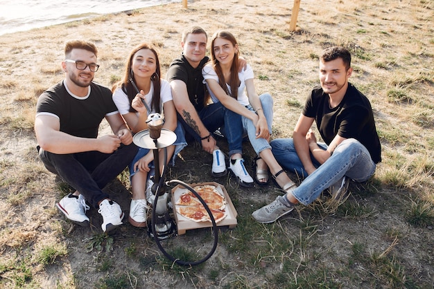 Młodzi ludzie jedzący pizzę i palący fajkę wodną na plaży