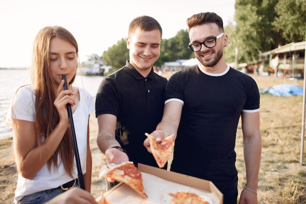 Młodzi ludzie jedzący pizzę i palący fajkę wodną na plaży