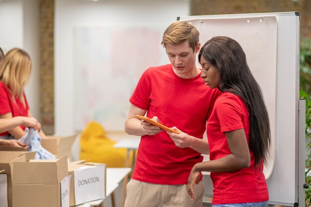 Bezpłatne zdjęcie młodzi ludzie w czerwieni wyglądają na zajętych pracą przy rozdzielaniu darowizn