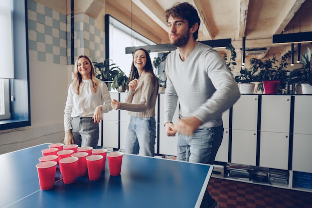 Młodzi ludzie współpracownicy grający w piwnego ping ponga w nowoczesnym biurze