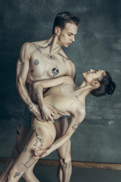 Bezpłatne zdjęcie młodzi nowocześni tancerze baletowi z tatuażami na ciałach pozują na szarym tle studyjnym