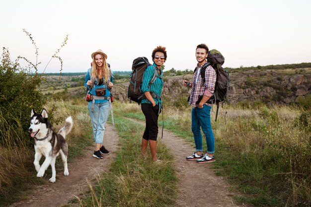 Młodzi przyjaciele z plecakami i husky, uśmiechając się, podróżując po kanionie