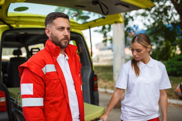 Młodzi ratownicy medyczni wyciągają nosze karetki z samochodu Sanitariusze w mundurach wyciągają nosze z karetki