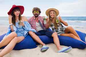 Bezpłatne zdjęcie młodzi uśmiechnięci przyjaciele na wakacjach, siedząc w workach fasoli na imprezie na plaży