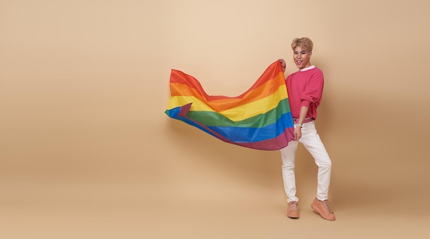 Bezpłatne zdjęcie młodzieżowa azjatycka osoba transpłciowa lgbt z tęczową flagą wyizolowaną na tle nagiego koloru mężczyzna z koncepcją flagi dumy gejowskiej