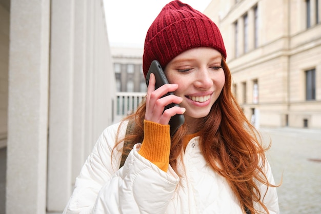 Mobilne łącze szerokopasmowe i uśmiechnięci ludzie młoda ruda kobieta spaceruje po mieście i rozmawia przez telefon komórkowy