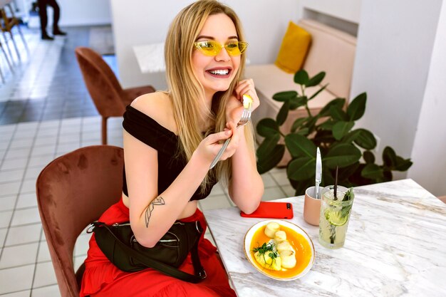Moda kryty portret młodej modnej hipster kobiety blondynka pozowanie w kawiarni nowoczesnej hipster, poranne śniadanie.